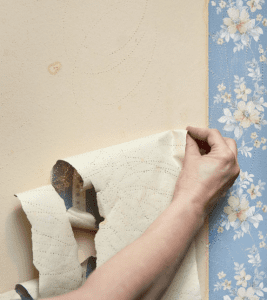 Hand removing wallpaper from wall.